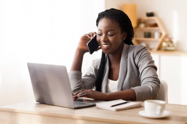 İş hayatı. Afrikalı iş kadını cep telefonuyla konuşuyor ve modern ofiste dizüstü bilgisayarla çalışıyor. Boşluğu kopyala