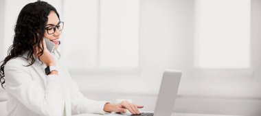 İş görüşmesi. Mutlu Meksikalı kadın cep telefonuyla konuşuyor, müşteriye danışıyor ve dizüstü bilgisayar kullanıyor. Boşluğu kopyala