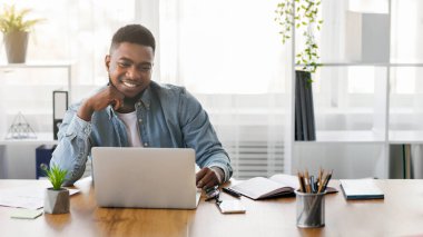 Başarılı bir proje. Gülümseyen Afrikalı Amerikalı iş adamı iş yerinde dizüstü bilgisayara bakıyor ve kişisel başarının keyfini çıkarıyor..