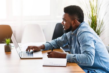 Ofiste dizüstü bilgisayar kullanırken not alan Afrikalı işçiler, boş alanlı yan görünüm