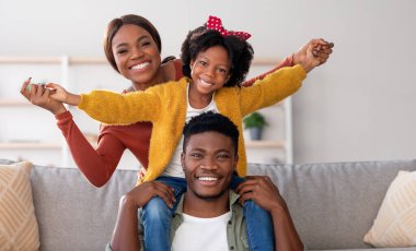 Family Leisure. Happy Black Mom, Dad And Little Daughter Having Fun At Home Together, African American Father, Mother And Cute Female Child Playing In Living Room And Smiling At Camera, Free Space