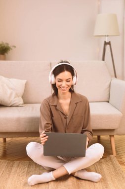 İçişleri Bakanlığı. Dizüstü bilgisayarda çalışan, yerde oturup kulaklıkla müzik dinleyen mutlu bir kız.