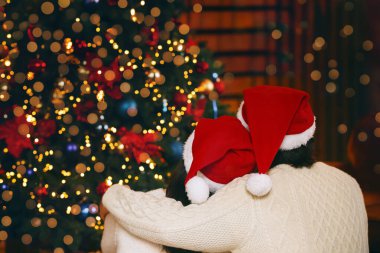 Noel Baba şapkalı mutlu evli çift Noel ağacına, arka manzaraya, kopyalama alanına bakıyor.