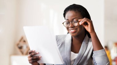 Evrak işi kavramı. Ofiste Mali Raporu okuyan mutlu Afrikalı iş kadını, sonuçtan memnun..