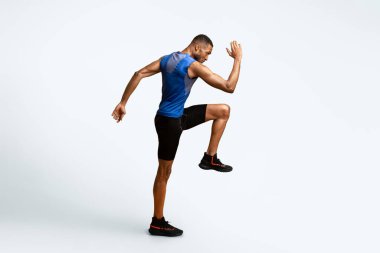 Yüksek dizler. Enerjik afro adam spor yapıyor, bacağını kaldırıyor ve kolunu sallıyor.
