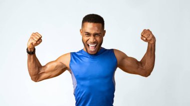 Yes You Can. Emotional black sportsman screaming, raising clenched fists in the air, yellow studio wall, panorama