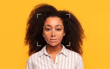 Kıvırcık saçlı genç siyah bir kadın sarı arka planda duruyor. Yüz tanıma teknolojisi yüzünü tarıyor..