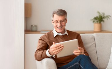 Emeklilik hayatı. Mutlu Olgun Adam, Tablet Bilgisayar kullanarak evdeki koltukta oturup iş haberleri okuyor. Seçici Odaklanma, Boşluğu Kopyala