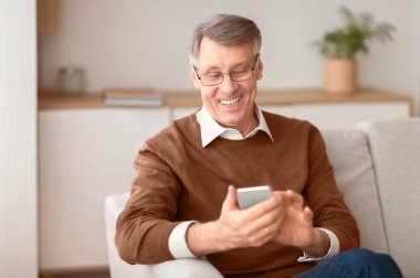 Üst düzey beyefendi cep telefonu kullanıyor. Evdeki koltukta oturmuş oyunlar oynuyor. Seçici Odaklanma