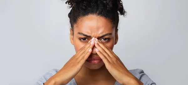 stock image Exhausted afro woman rubbing nose bridge, suffering from antritis, grey background