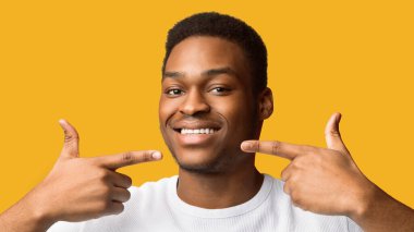 Sağlık kavramı. Yakışıklı siyah adam gülümsüyor ve parmaklarıyla dişleri ve ağzı işaret ediyor, panorama, telif alanı
