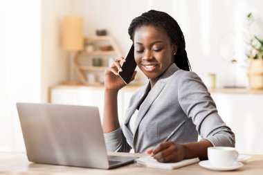 Afro iş kadını telefon görüşmesi yaparken notlar alıyor, Modern Ofiste masada oturuyor, Seçici Odaklanma