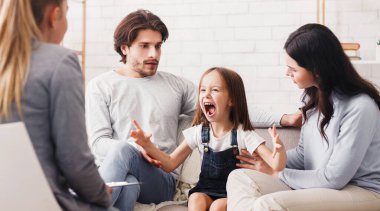 Sorunlu çocuk. Şok geçirmiş ebeveynler çığlık atan küçük kızlarını psikolog muayenesinde sakinleştiriyor, davranışlarıyla ilgili problemleri var.
