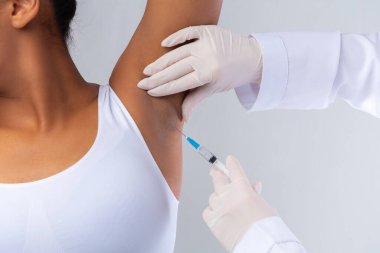 Doktor koltukaltı bölgesinde hiperhidroz, kesilmiş, siyah kadın koltukaltına karşı kas içi botulinyum iğnesi yapıyor.