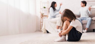 Aile çatışması. Küçük bir kız, anne babası evde kavga ettikten sonra ağlıyor, kafası aşağıda oturuyor, yüzünü dizlerine gizliyor, seçici bir şekilde odaklanıyor.