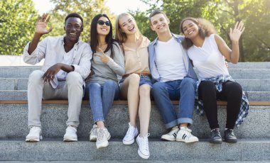 Mutlu arkadaşlar uluslararası öğrenciler yaz şehrinde birlikte vakit geçiriyorlar, merdivenlerde oturup gülümsüyorlar.