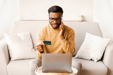 Memnuniyetsiz siyahi adam bankayı arıyor. Evde bilgisayardan kredi kartı alışverişi yapıyor.