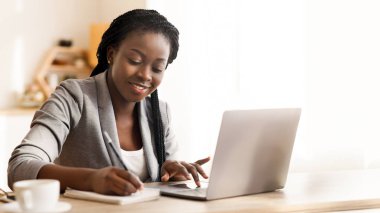 Ofiste çalışan siyahi bir girişimci, dizüstü bilgisayarda yazı yazıyor ve notlar alıyor.