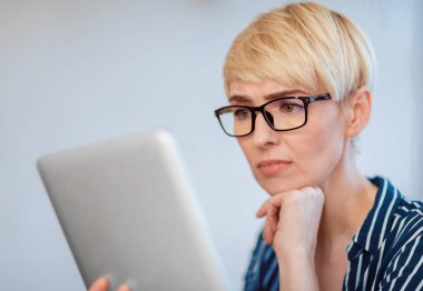 Hoşnutsuz Olgun İş kadını Gözlüklü Dijital Tablet Okuyan İş Haberleri Salonunda Oturuyor. Seçici Odaklanma