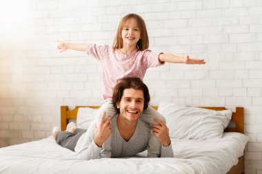 Baba ve kızı sabahları evde birlikte vakit geçiriyorlar. Mutlu küçük kız babasının omuzlarında oturuyor, elleri havada, babası yatakta yatıyor, boş yer var.