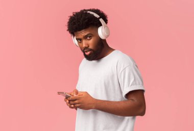 Akıllı telefon için güzel bir müzik uygulaması. Pembe arka planda telefon kullanan kablosuz kulaklıklı genç bir zenci.