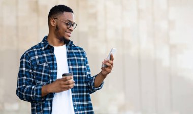 Teknoloji Konsepti. Genç başarılı afro tasarımcı telefonda dostlarından iyi haberler okuyor ve sabah kahvesinin tadını çıkarıyor.