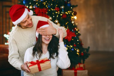 Sevgi dolu genç bir adam karısına sürpriz bir hediye veriyor, gözlerini kapatıyor, Noel 'i evde kutluyor.