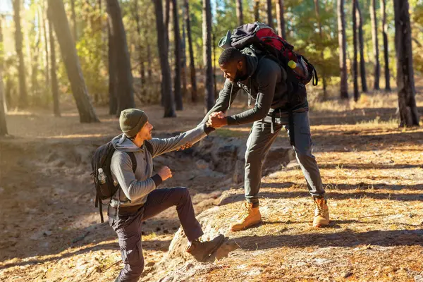 İki arkadaş kırsalda yürüyüş yapıyor, siyahi adam beyaz adamın yokuş yukarı çıkmasına yardım ediyor, arkadaşlık kavramı.