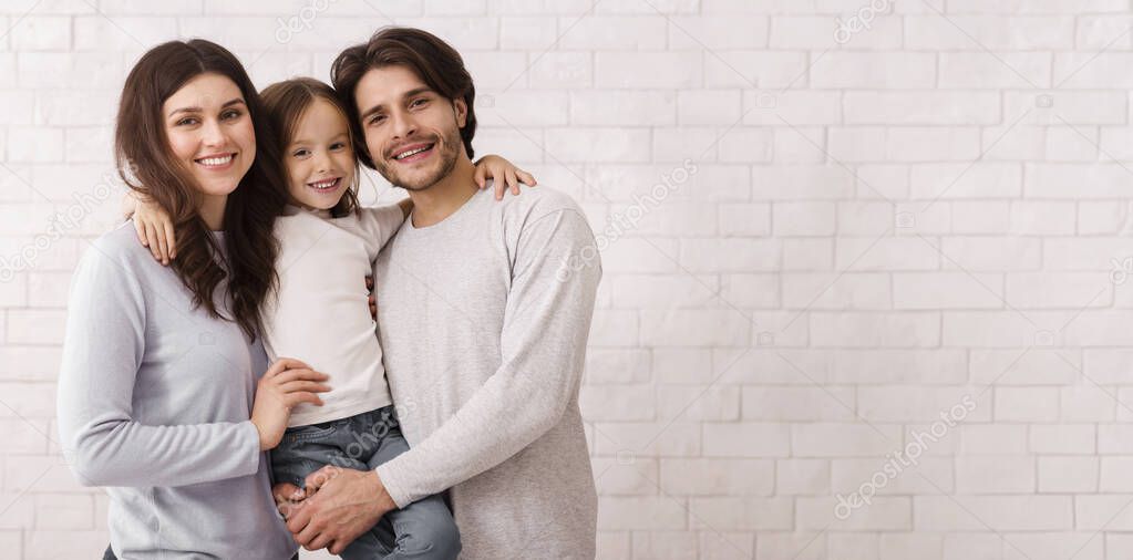 Caring Family. Portrait Of Loving Parents With Their Cute Little Daughter On Hands Posing Over White Brick Wall Background Indoors, Copy Space