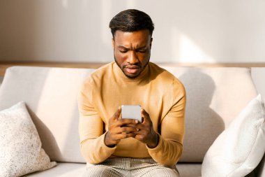Smaprtphone tutan hoşnutsuz Afro-Amerikalı adam ve evde oturan somurtkan kitap okuyan adam. Seçici Odaklanma