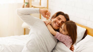 Sevimli küçük kız uyandıktan sonra neşeli babasına sarılıyor, yatak odası arka planı, birlikte mutlu.