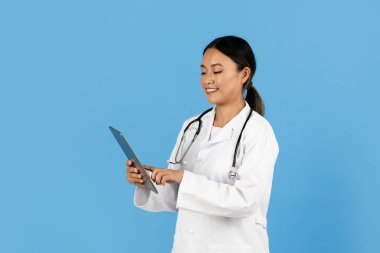Beyaz önlüklü ve steteskoplu bir sağlık uzmanı, cihazla mavi arka planda gülümseyen ve etkileşime geçen bir tabletle ilgilenir..