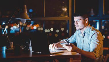 İş Başvurusu. Genç Girişimci cep telefonu mesajlaşması kullanıyor geceleri modern ofiste dizüstü bilgisayarla çalışıyor. Boş Alan