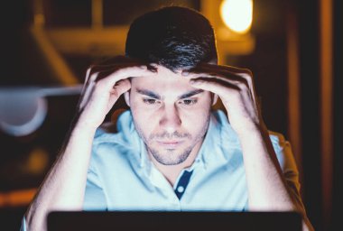 Düşünceli iş adamı laptopa bakıp zor görevlere odaklanmayı düşünüyor. Geceleri modern ofiste oturuyor.