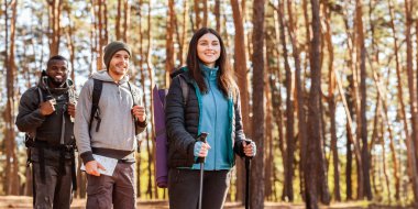Gülümseyen çoklu etnik yürüyüşçüler çam ormanlarının arka planında kameraya bakıyorlar.