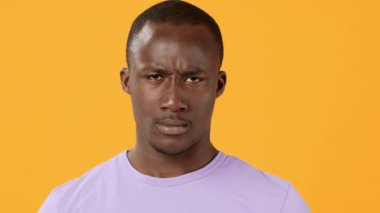 Genç bir adam ciddi bir ifadeyle, parlak turuncu bir arkaplanı doğrudan izleyiciye işaret ederek güvenle ayakta duruyor. Duruşu kararlılığını ve bağlılığını ifade ediyor..