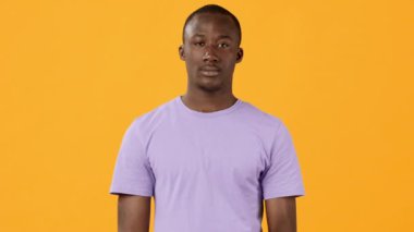 Mor gömlekli genç bir adam parmağını dudaklarına dayayıp sessizlik istiyor. Parlak sarı arka plan neşeli bir zıtlık ekler, o anın neşeli havasını arttırır..