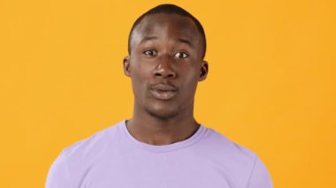 Genç bir adam canlı sarı bir arkaplan karşısında duruyor, ağzı hafifçe açık şaşırmış bir yüz ifadesi çiziyor, neşeli ve çekici bir atmosfer yaratıyor..