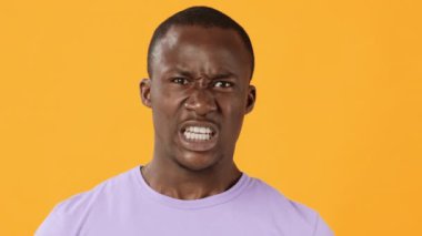 Genç bir erkek gözle görülür şekilde kızgın, parlak turuncu bir arkaplana karşı yoğun duygularla bağırıyor, güçlü duygularını dinamik bir şekilde vurguluyor..