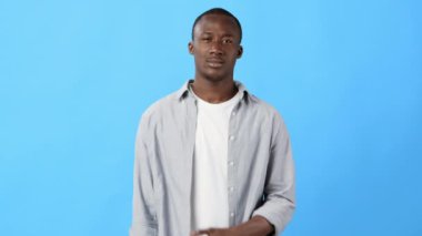 Katı mavi bir arka fonun önünde duran bir adam, gözle görülür şekilde sıkıntılı ve göğsünü tutuyor, fiziksel rahatsızlık ya da acı hissediyor olabileceğini öne sürüyor..