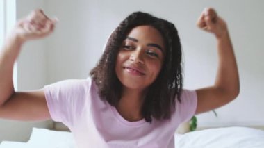 Afro-Amerikalı kadın, parlak yatak odasında dans ederek mutluluğunu ifade ediyor. Sabah ışığı altında kaygısız bir anın tadını çıkarıyor..