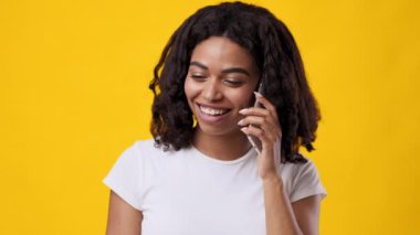 Akıllı telefonuyla konuşurken kıvırcık saçlı genç bir Afrikalı Amerikalı kadın, o ana enerji katan canlı sarı bir ortam yaratıyor..