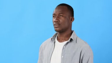 Bir adam yüzünü kaşırken acı dolu bir yüz ifadesi gösterir. Mavi arka plan, gözle görülür rahatsızlığı arttırır. İlişkili bir mücadele anını yakalar..