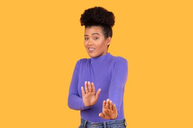 The young woman smiles and holds her hands up with a playful expression, standing in front of a vibrant yellow background. Her casual style adds to the lighthearted atmosphere of the moment. clipart