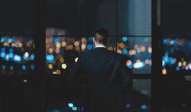 Başarılı iş adamı Panoramik Pencerenin yanında duruyor Modern Ofiste Gece Şehir Manzarasına bakıyor. İş Başarı Konsepti