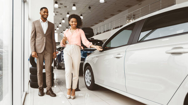 Покупаю машину. Афроамериканский бизнесмен выбирает автомобиль с женщиной-дилером, идущей в дилерский магазин. Озил, пустое пространство