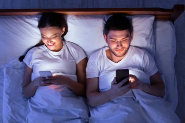 Couple Using Smartphones Ignoring Each Other Lying In Bed At Home At Night. Modern Relationship Problems. Top View