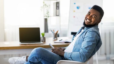 İş yerinde akıllı telefon kullanan, internete takılan veya arkadaşlarıyla mesajlaşan ve kameraya bakan neşeli Afro-Amerikan çalışanlarının portresi