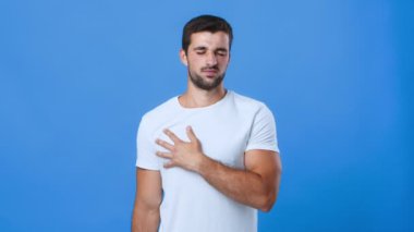 Genç bir adam bir eli göğsünde, düşünceli bir ifade sergiliyor. Basit bir beyaz gömlek giyiyor ve perde arkası da duygularını vurgulayan açık mavi bir renk..