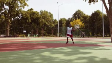 Genç bir Afrikalı Amerikalı, ağaçlarla çevrili canlı bir sahada basketbol topu sürüyor. Aydınlık bir öğleden sonra ve o dikkatle oyununu geliştirmeye odaklanıyor..